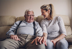 Old man sitting on couch with younger woman looking at him encouragingly