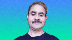 Man with mustache smirking with a blue/green background